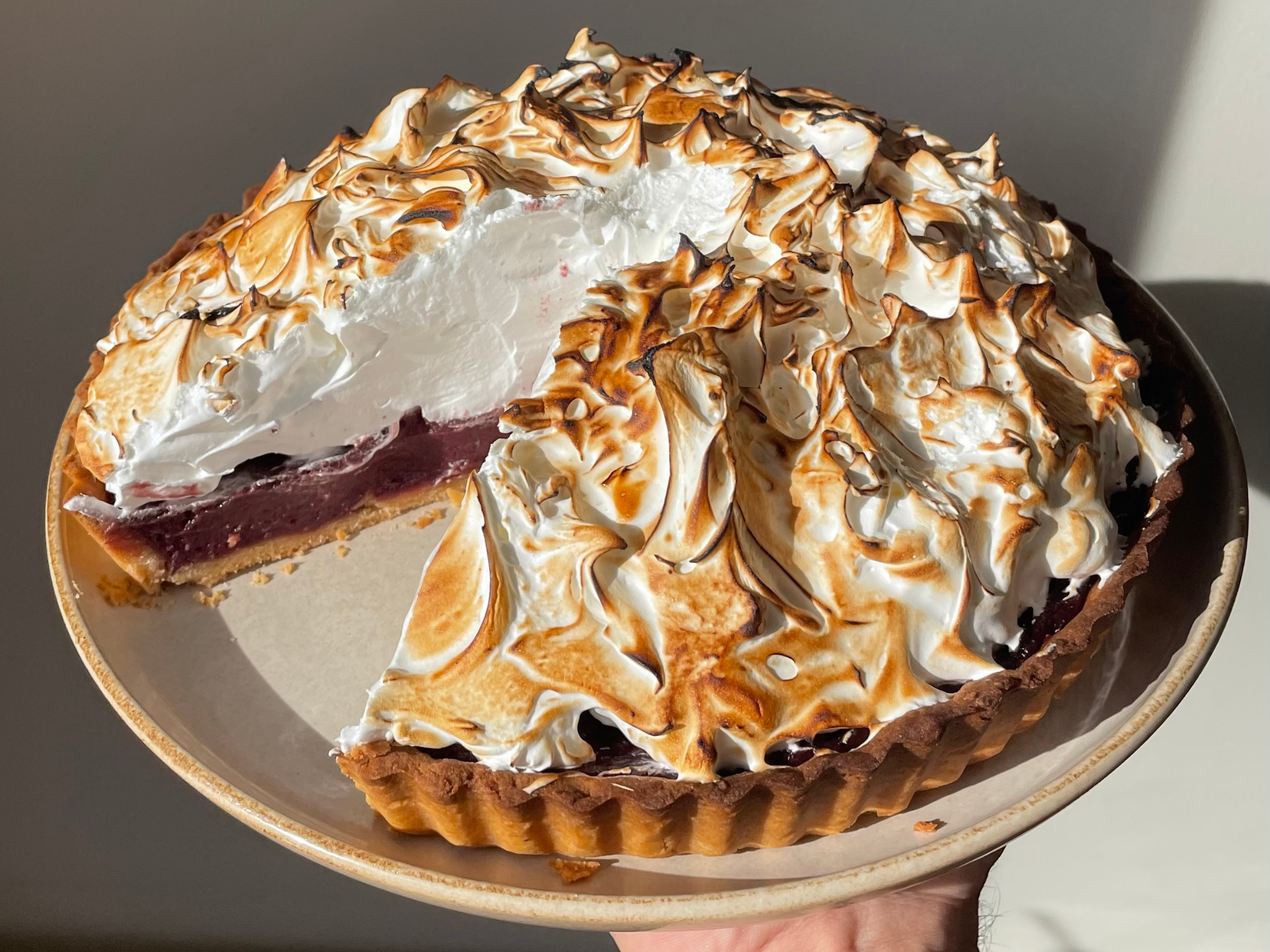Cherry yuzu meringue tart with a golden pastry crust and toasted meringue peaks, shown with one slice removed to reveal the vibrant cherry filling.