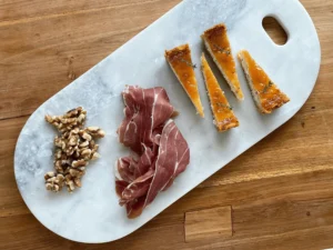 Sliced blue cheese cheesecake with quince glaze, served with prosciutto and walnuts on a marble board.